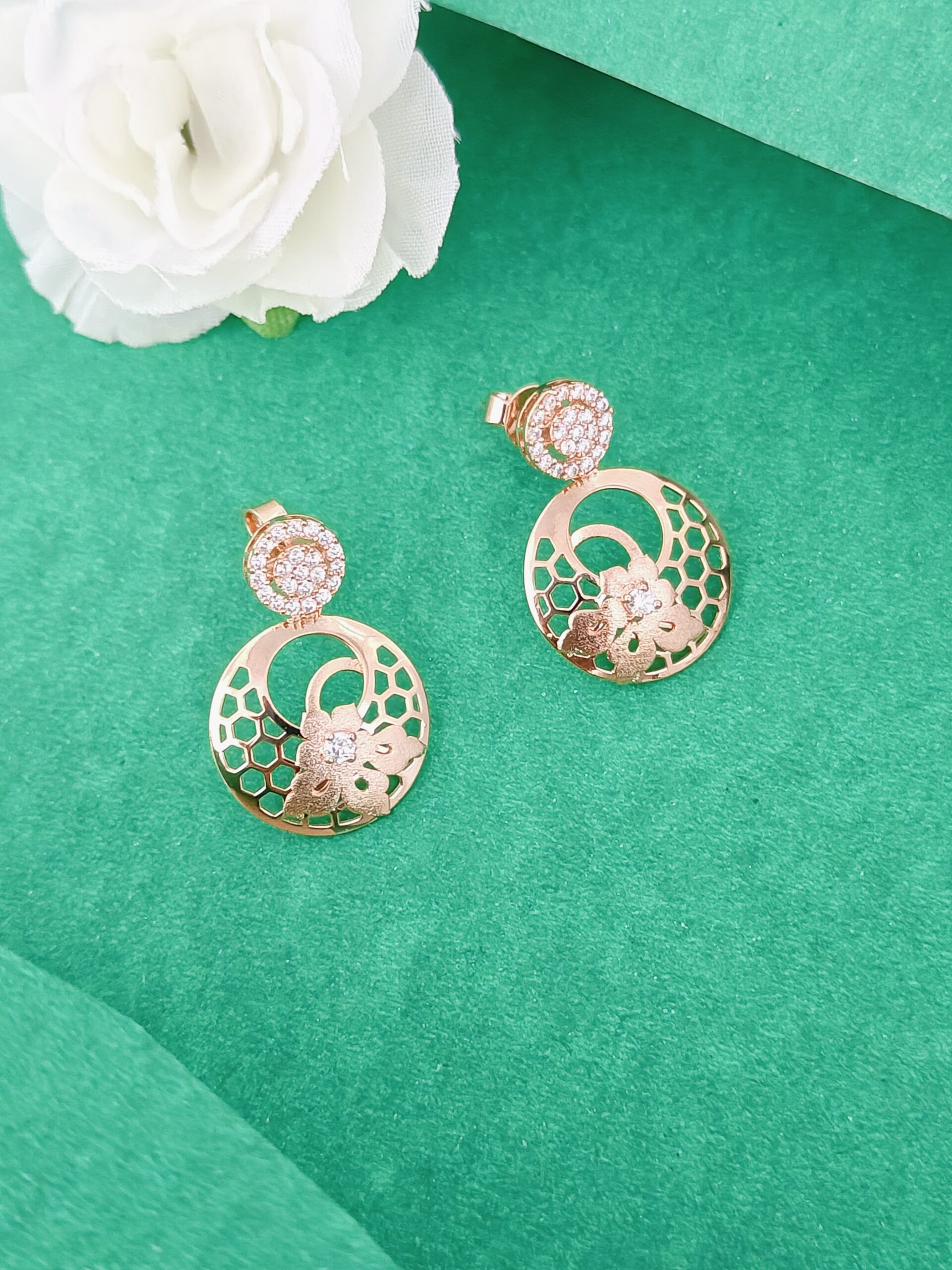 Gold earrings with floral design on a green surface with a white flower.